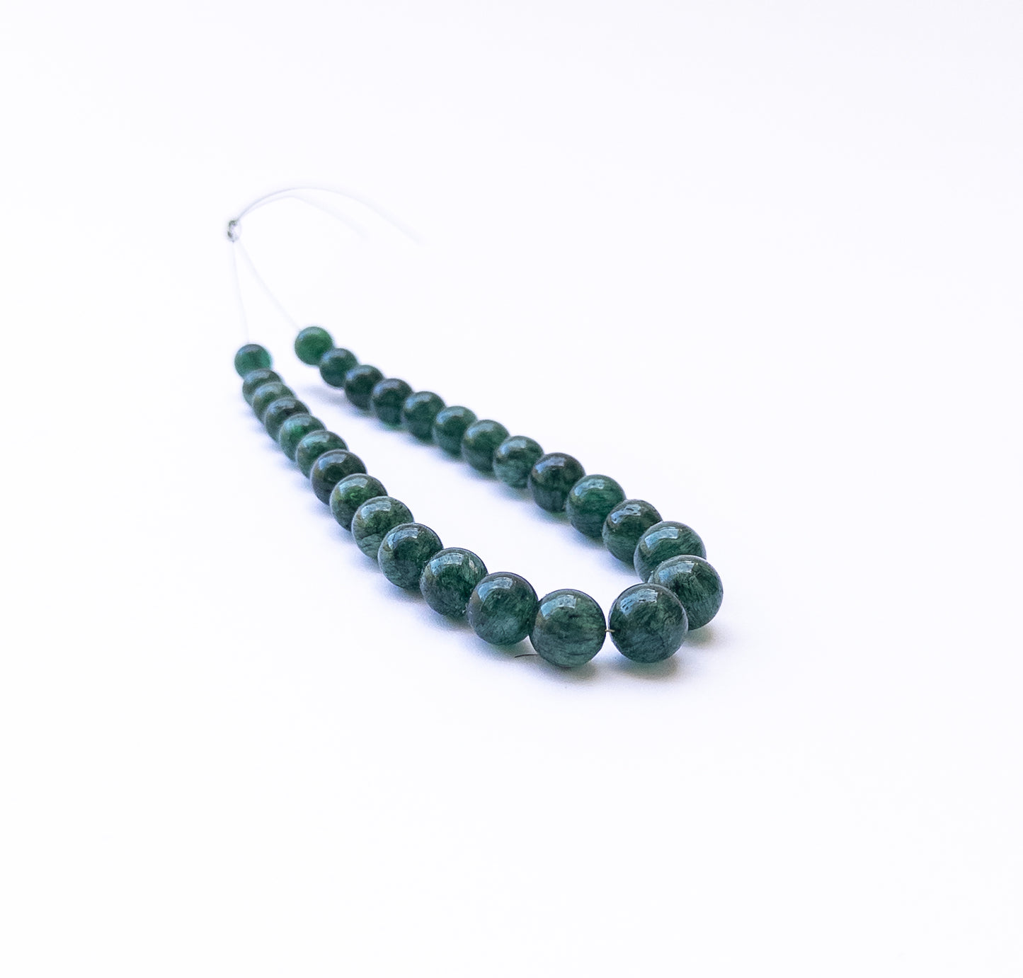 Emerald smooth round beads arranged in a strand showing deep green colour and polished surfaces.