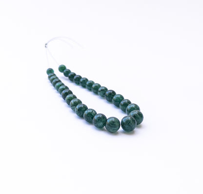 Emerald smooth round beads arranged in a strand showing deep green colour and polished surfaces.