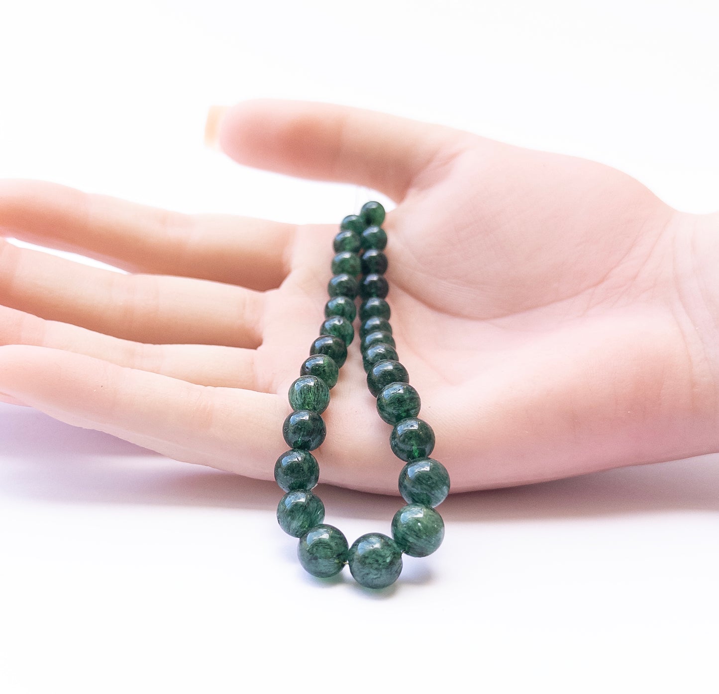 A person holds delicate pieces of Emerald smooth round beads, showcasing their shine.