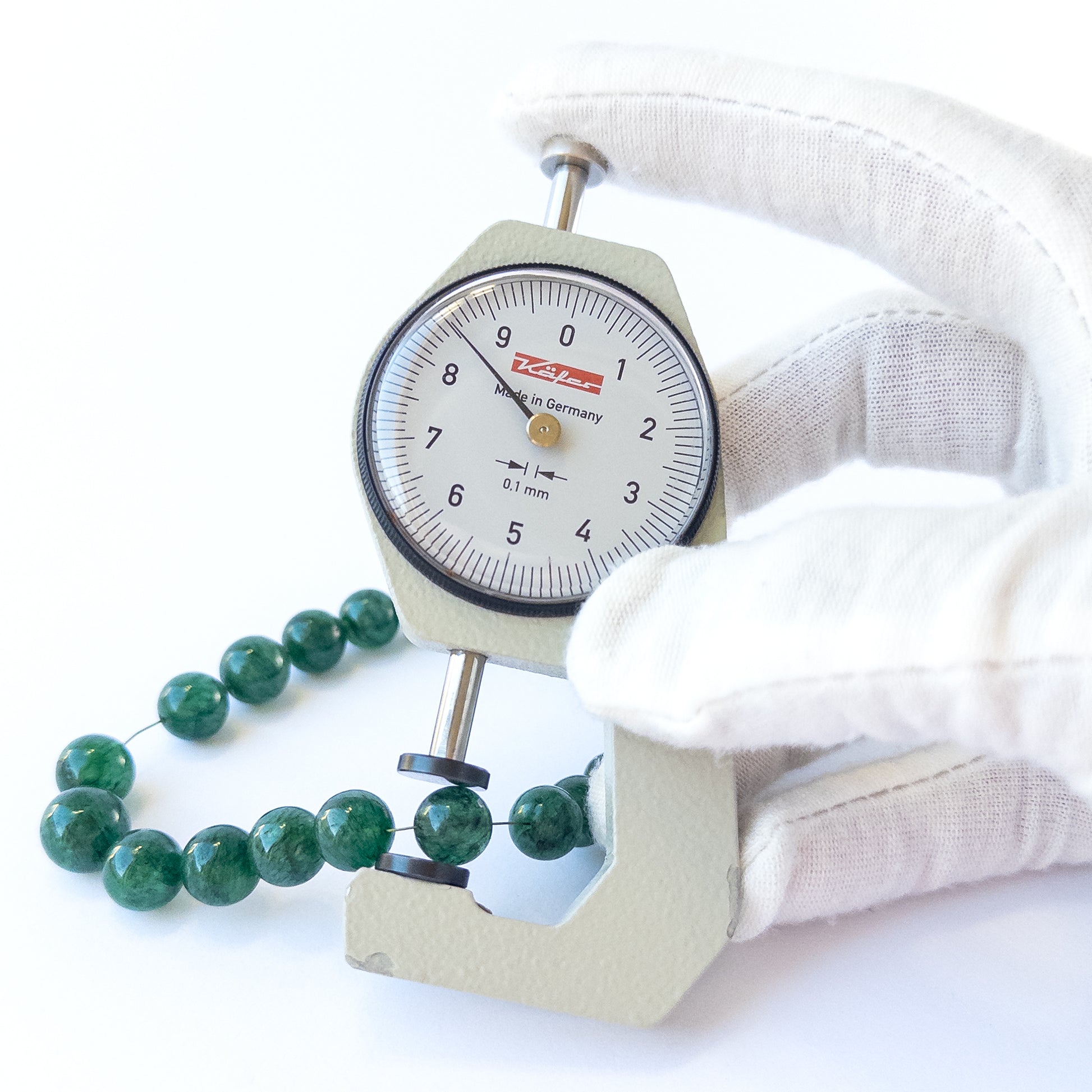 A coin is place near delicate pieces of Emerald beads for scale.