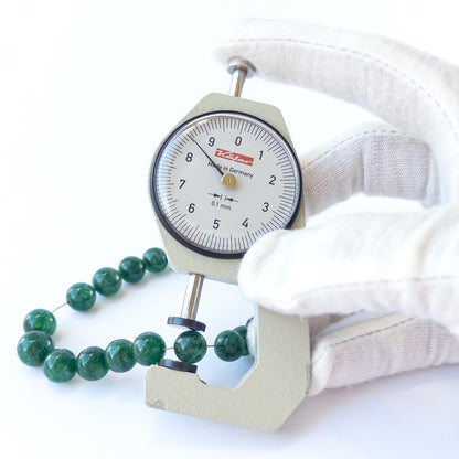 A coin is place near delicate pieces of Emerald beads for scale.