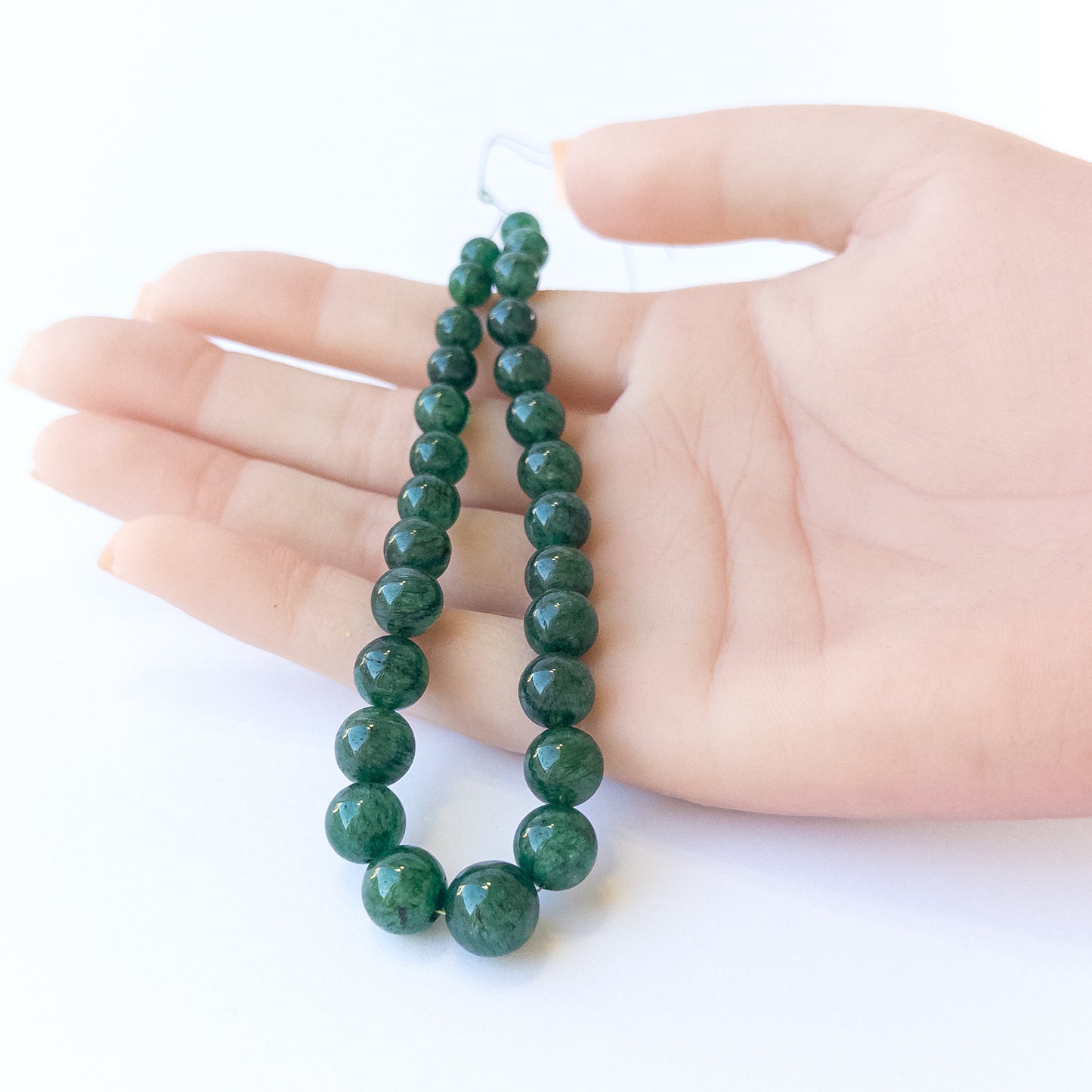 A person holds delicate strands of Emerald beads, showcasing their smooth round design.