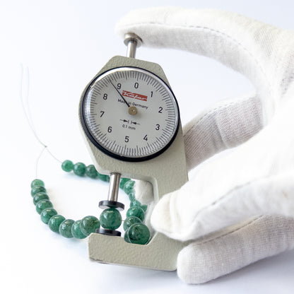 A dial gauge measures the Emerald smooth round 7–9mm gemstone.