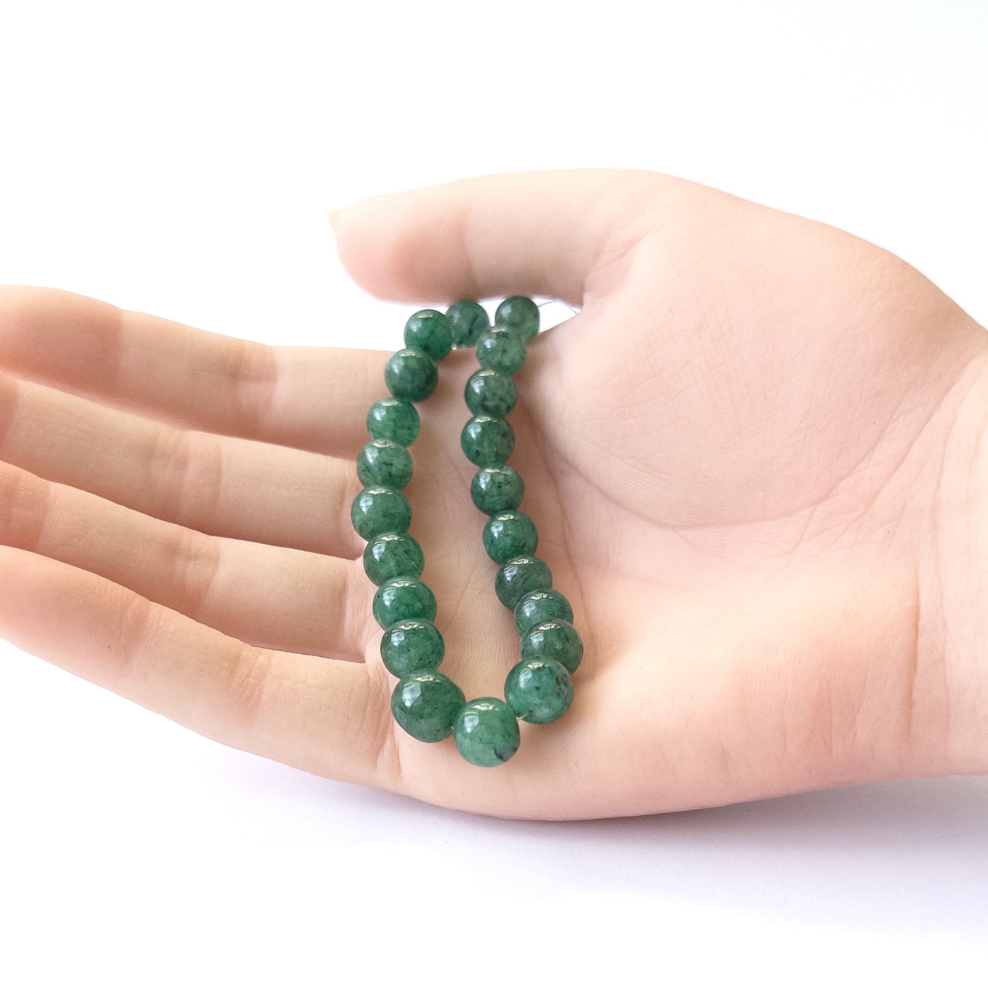 A person holds delicate pieces of Emerald beads, showcasing their smooth round design.