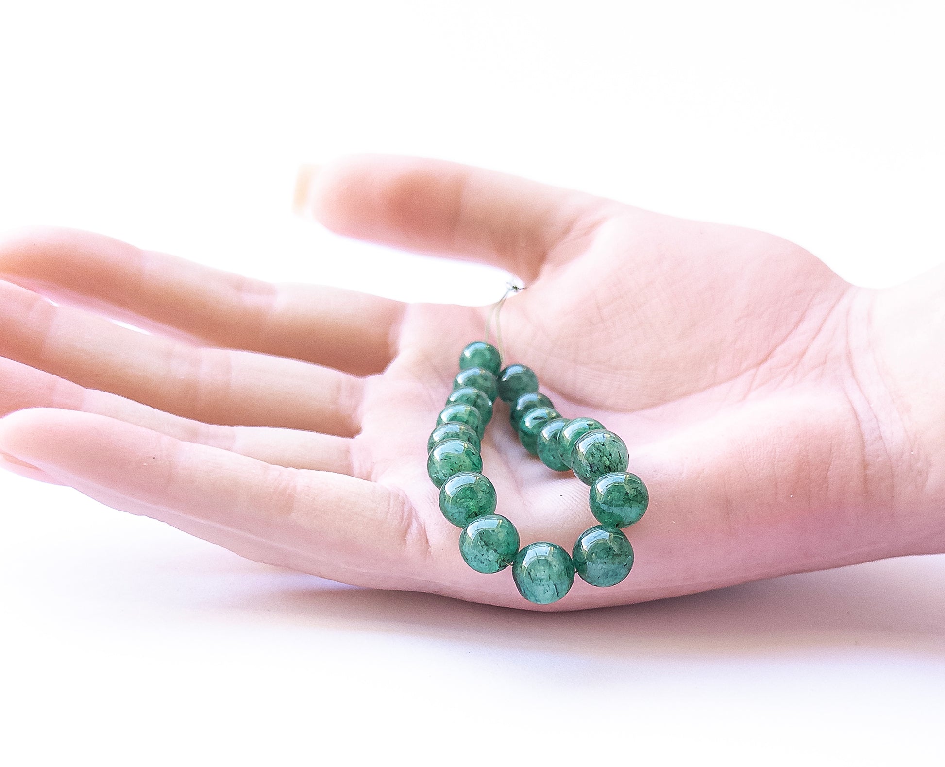 A person holds delicate pieces of Emerald smooth round beads, showcasing their shine.