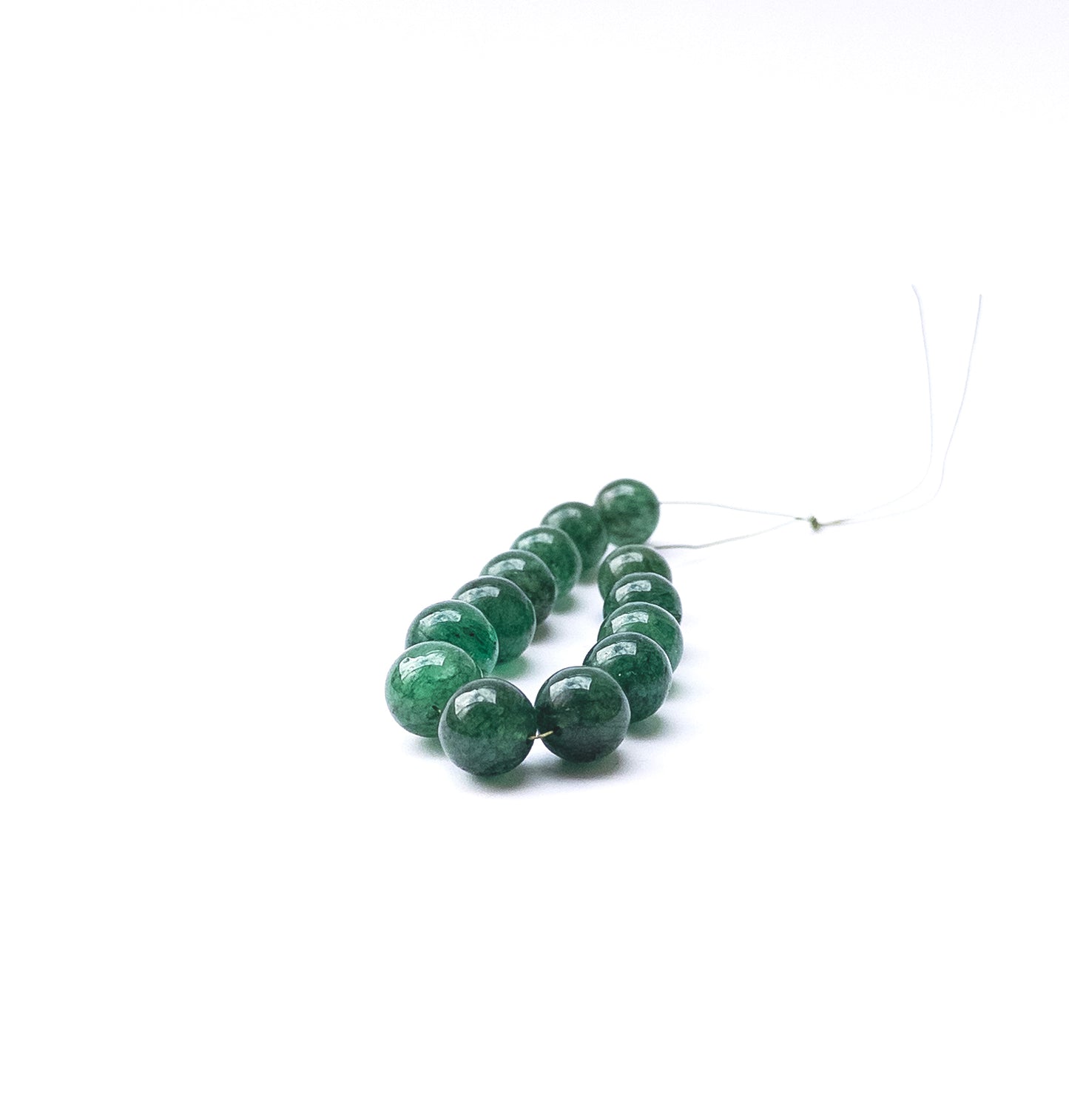 Emerald smooth round beads arranged in a strand showing deep green colour and polished surfaces.