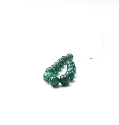 Emerald smooth round beads arranged in a strand showing deep green colour and polished surfaces.