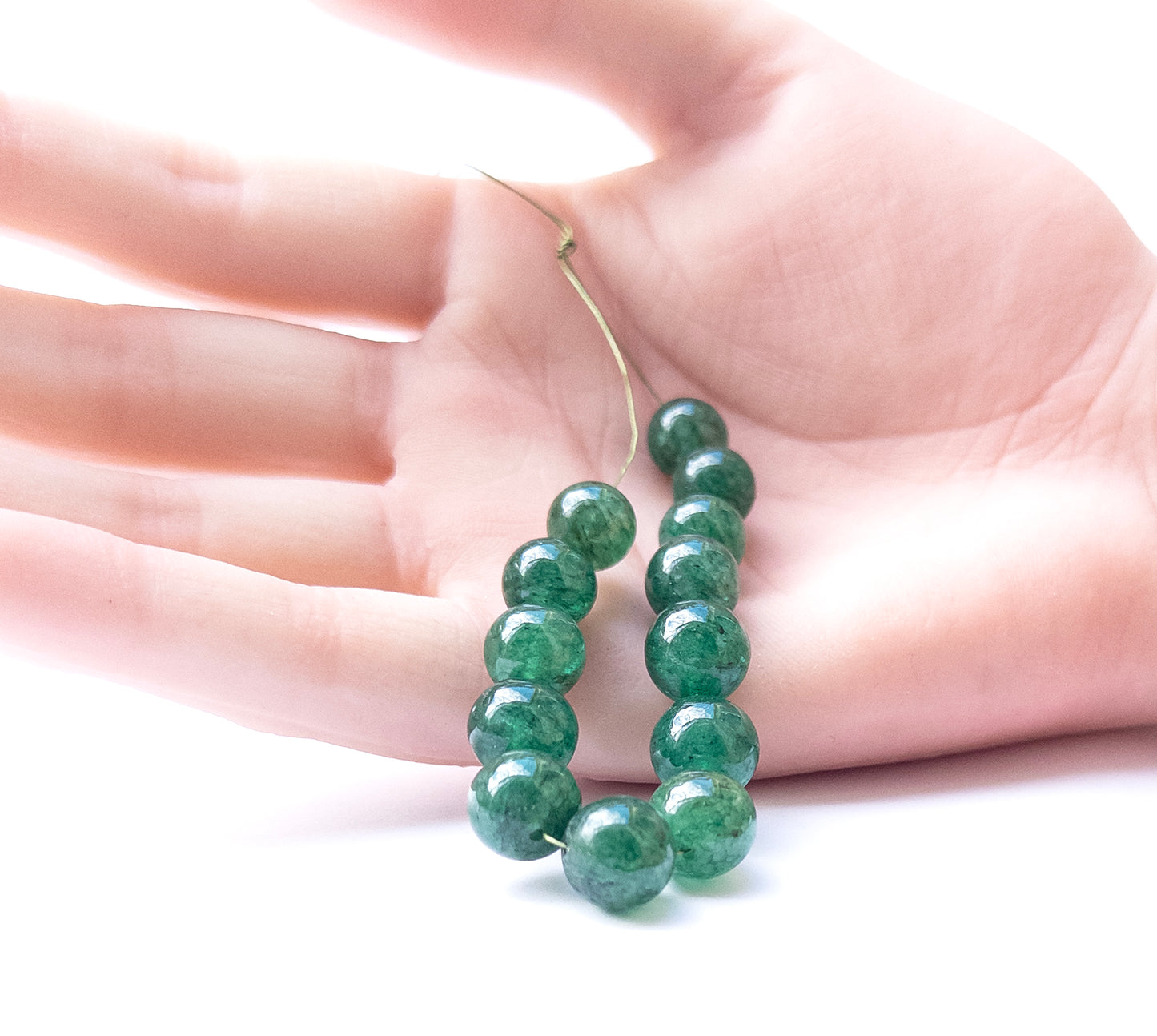 A person holds delicate pieces of Emerald smooth round beads, showcasing their shine.