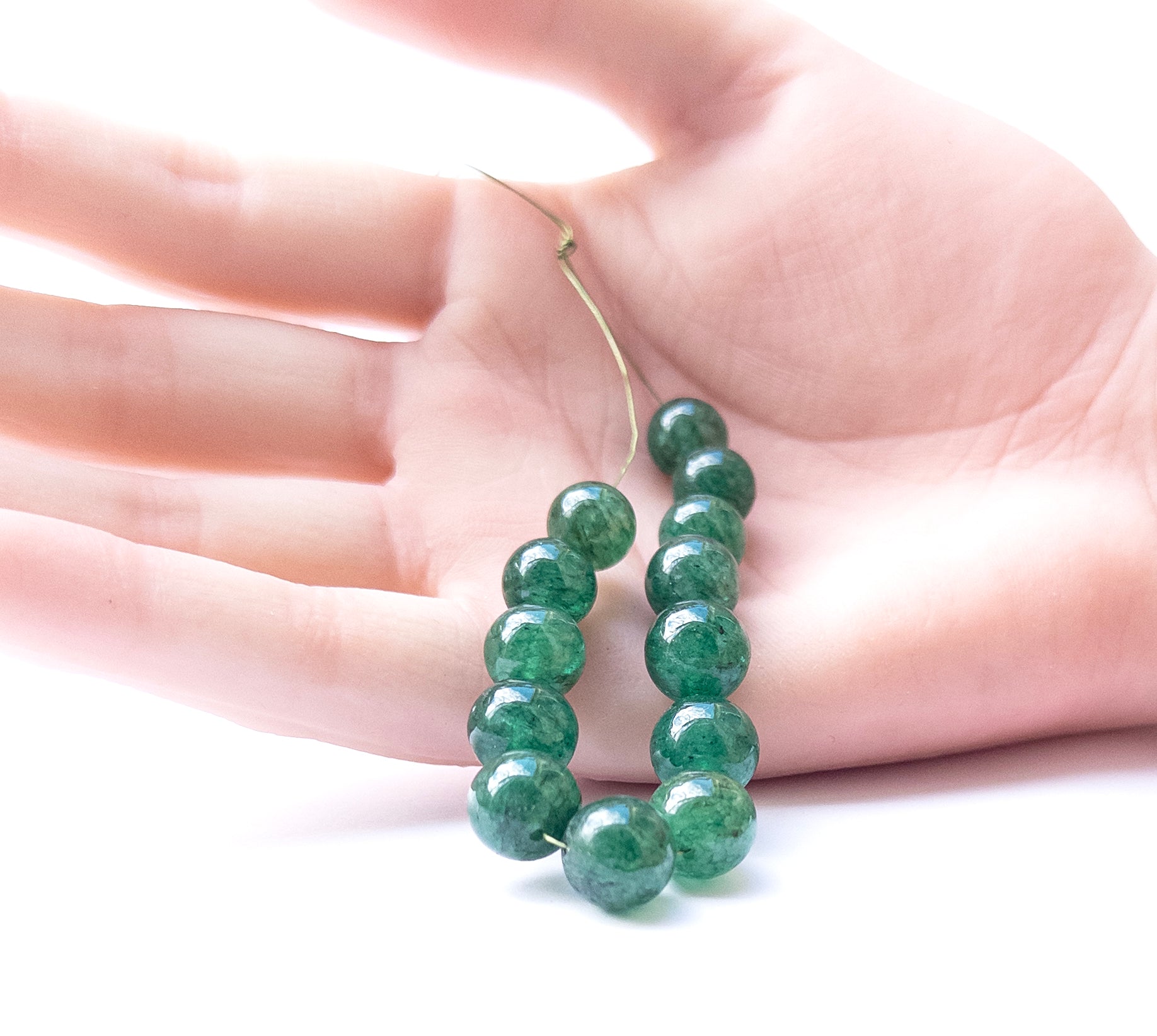 A person holds delicate pieces of Emerald smooth round beads, showcasing their shine.