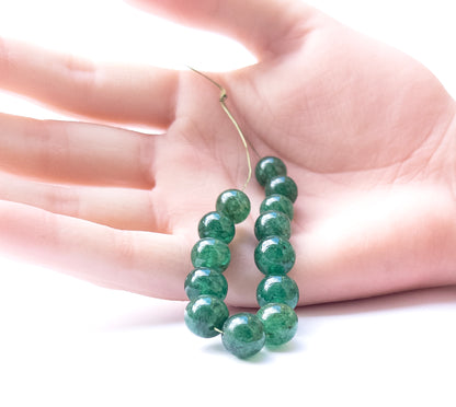 A person holds delicate pieces of Emerald smooth round beads, showcasing their shine.
