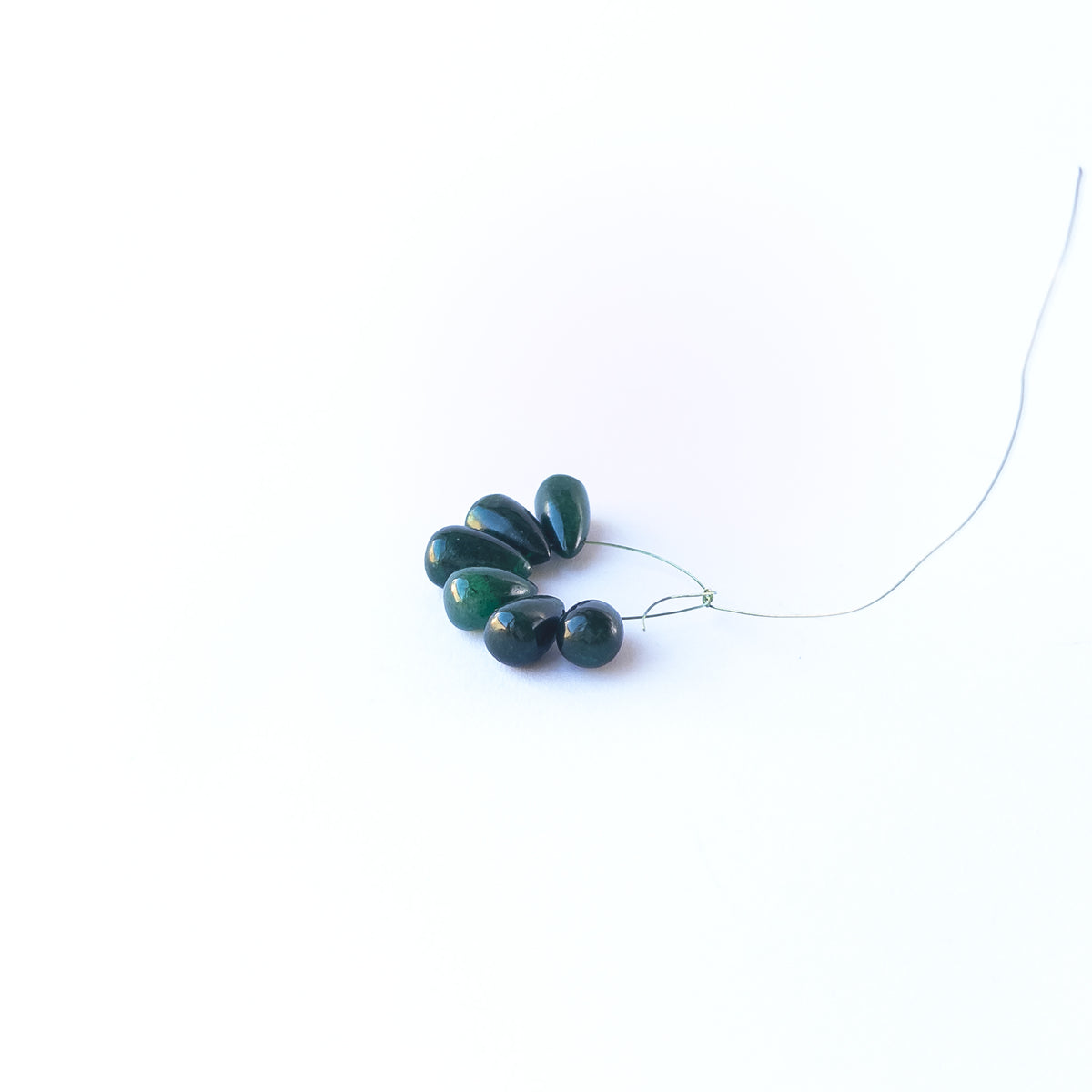 Emerald smooth briolette gemstone beads arranged in a mixed set showing soft green tones.