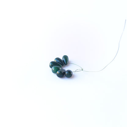 Emerald smooth briolette gemstone beads arranged in a mixed set showing soft green tones.