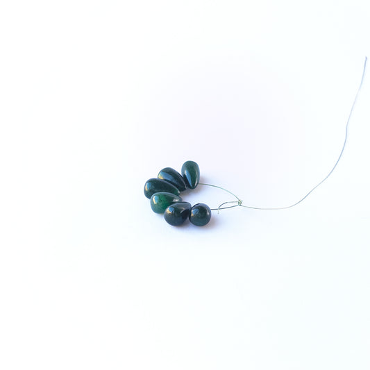 Emerald smooth briolette gemstone beads arranged in a mixed set showing soft green tones.