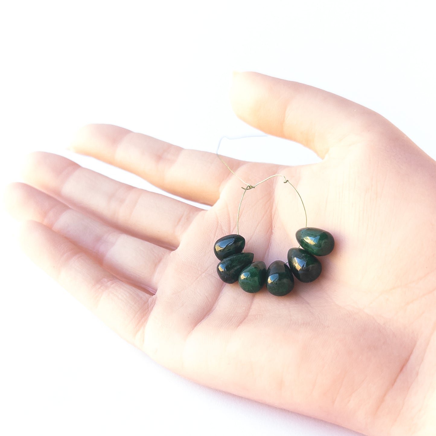 A person holds delicate Emerald briolette beads showcasing their smooth teardrop design.