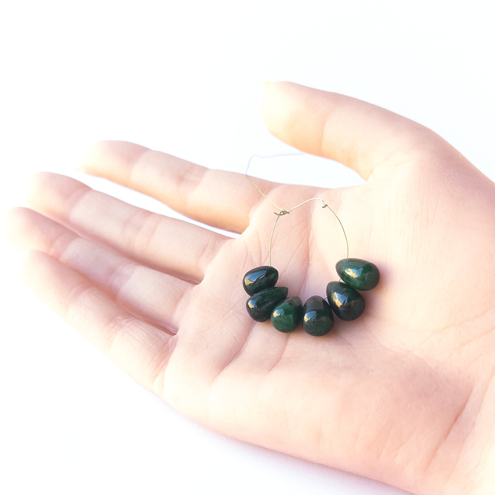 A person holds delicate Emerald briolette beads showcasing their smooth teardrop design.