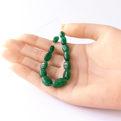 A person holds delicate pieces of Emerald beads, showcasing their smooth tumble design.