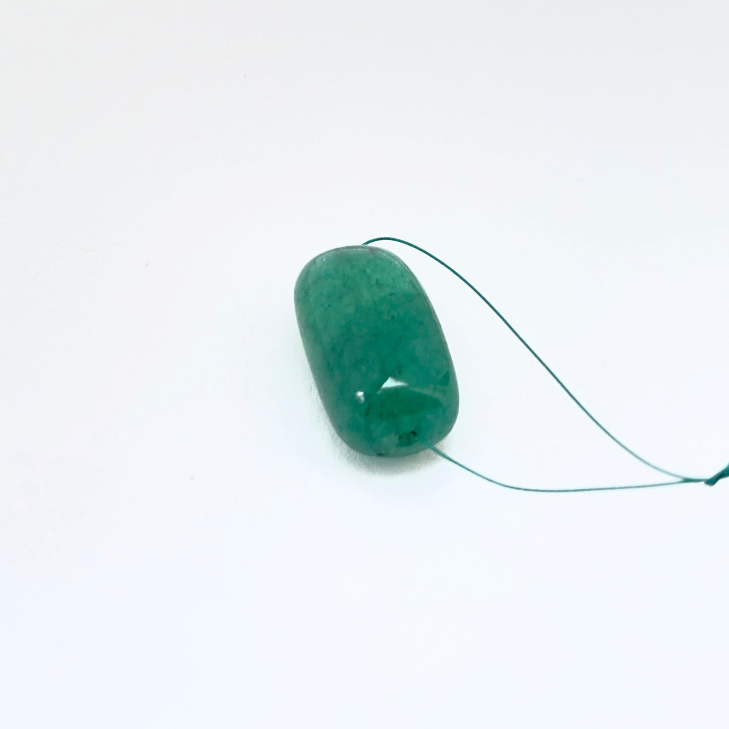 Single emerald tumbled drilled bead displayed to showcase shape and deep green tone.