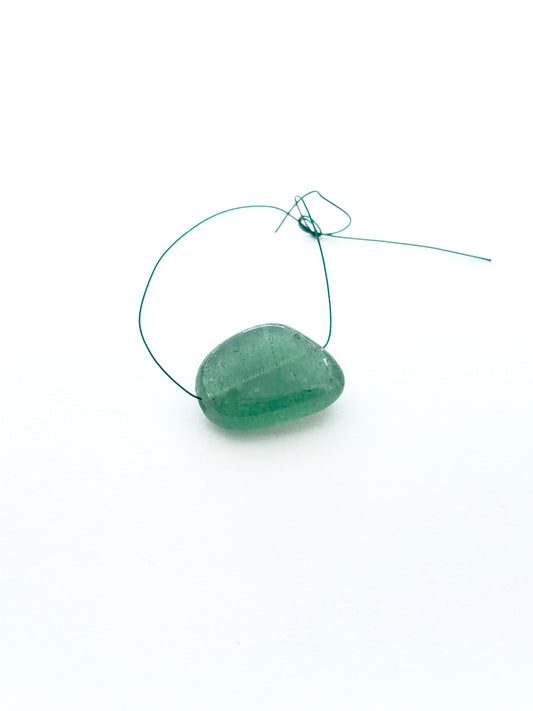 Single emerald tumble drilled bead displayed to showcase shape and rich green tone.