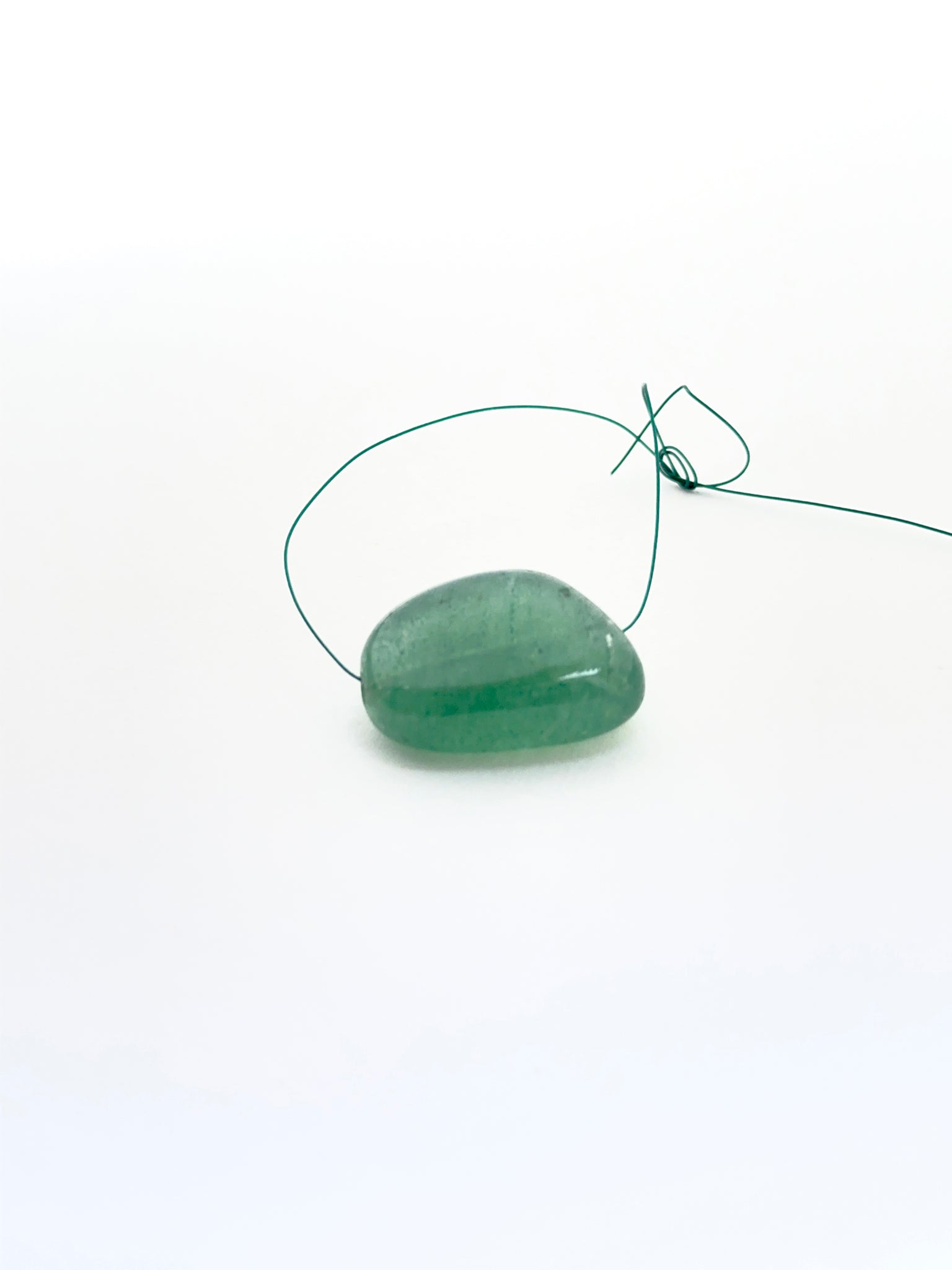 Emerald tumble bead photographed to show its organic form and suitability for jewellery making.