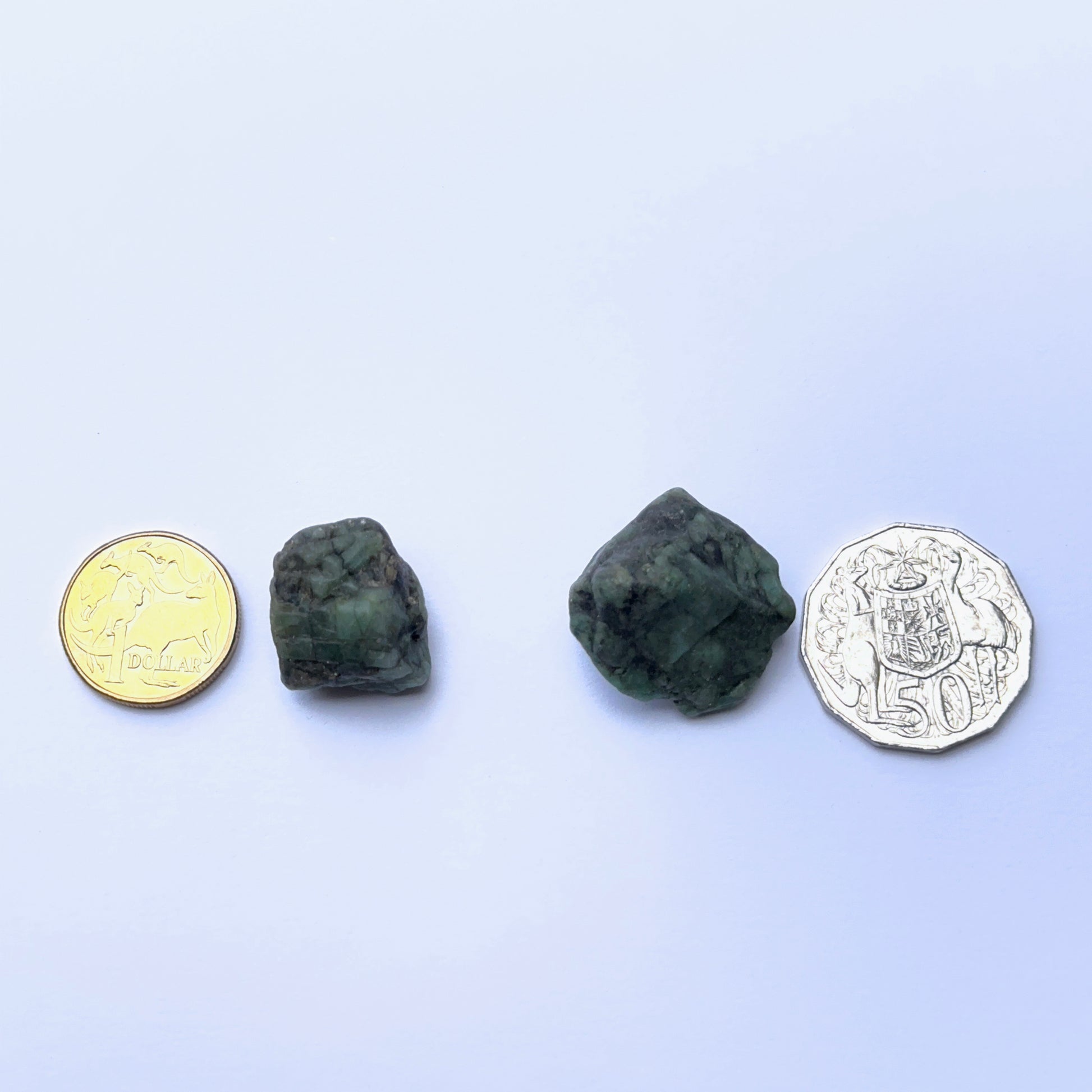 Close‑up of emerald rough stone highlighting raw structure and vibrant green colour next to coins to show scale.