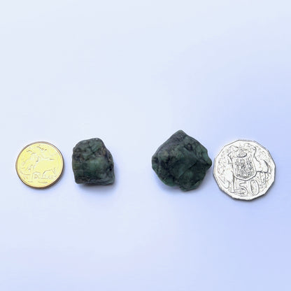 Close‑up of emerald rough stone highlighting raw structure and vibrant green colour next to coins to show scale.