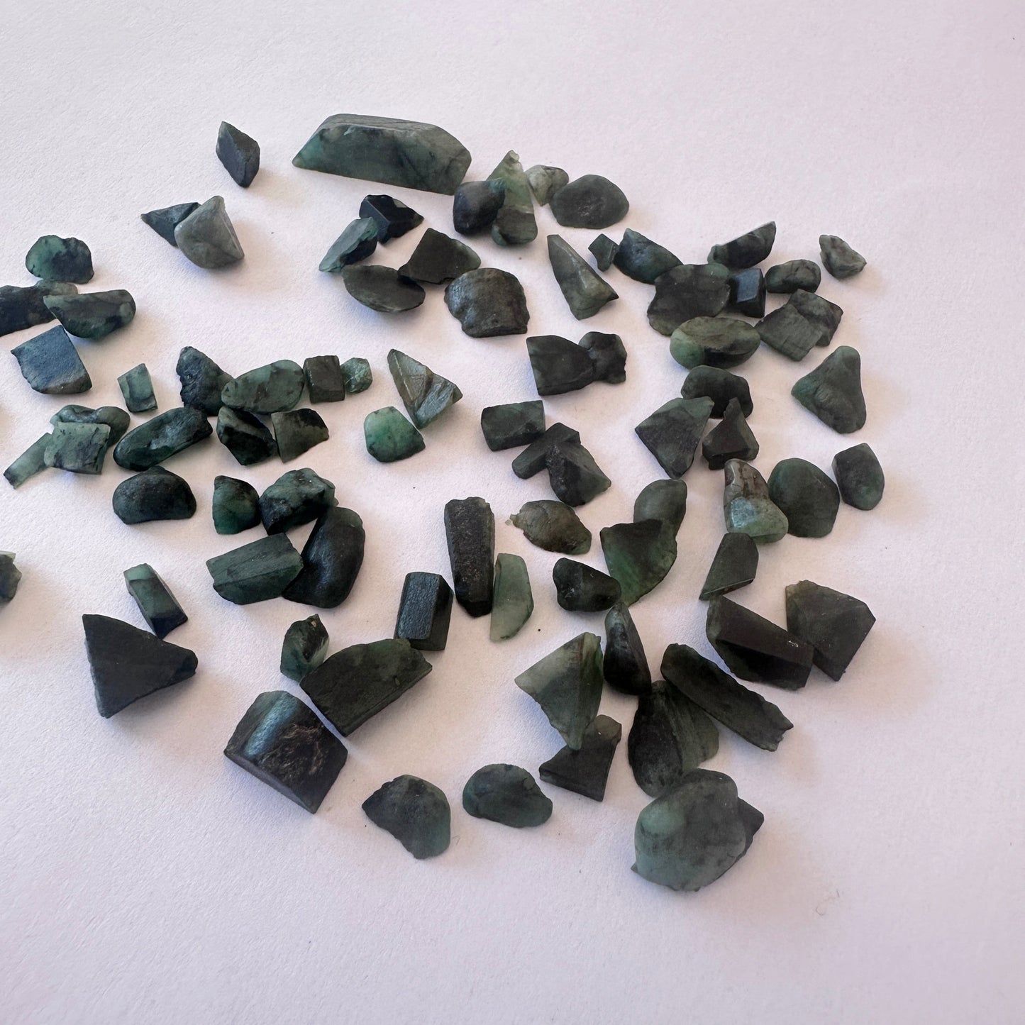Assorted Emerald rough pieces with vibrant hues and organic shapes arranged loosely.