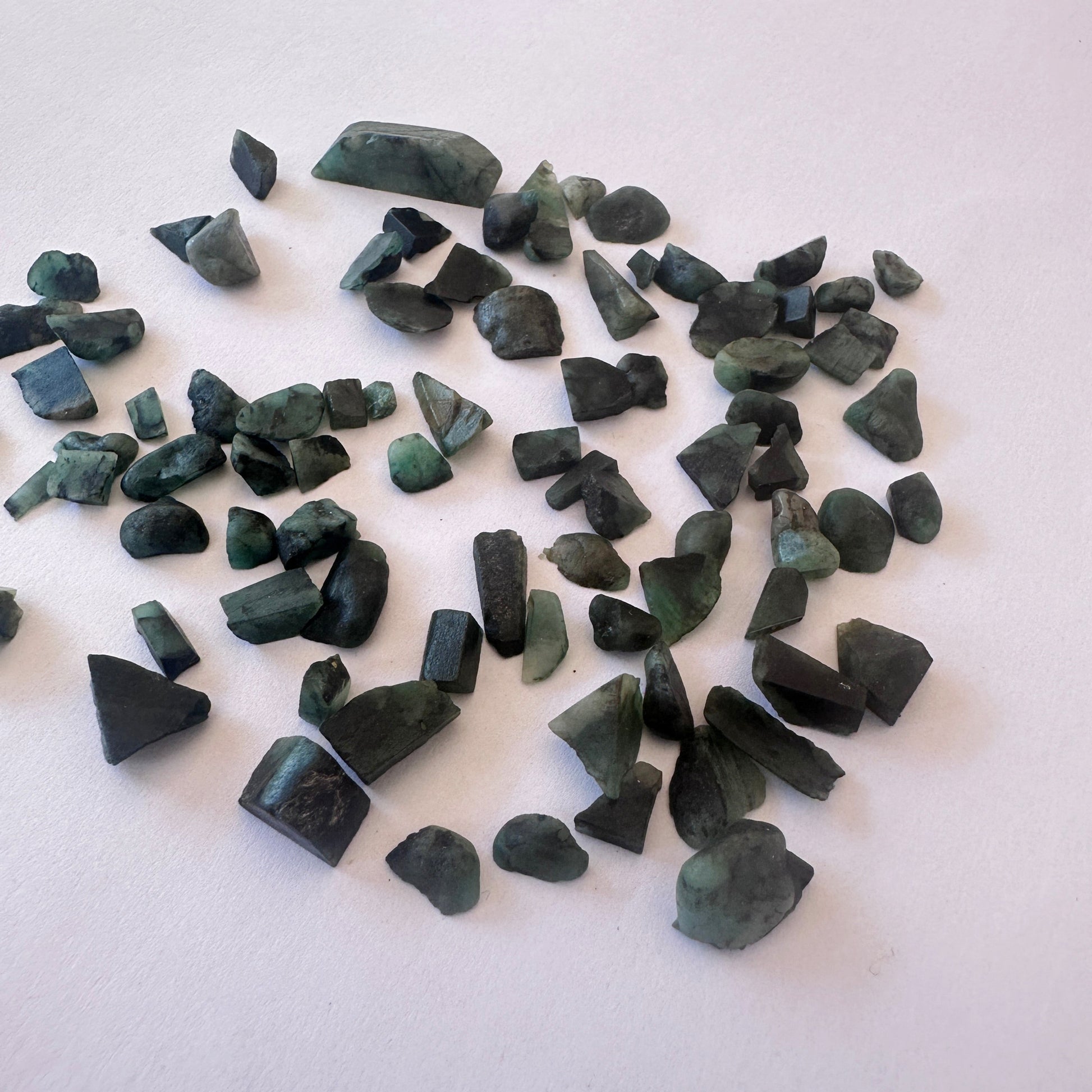 Assorted Emerald rough pieces with vibrant hues and organic shapes arranged loosely.