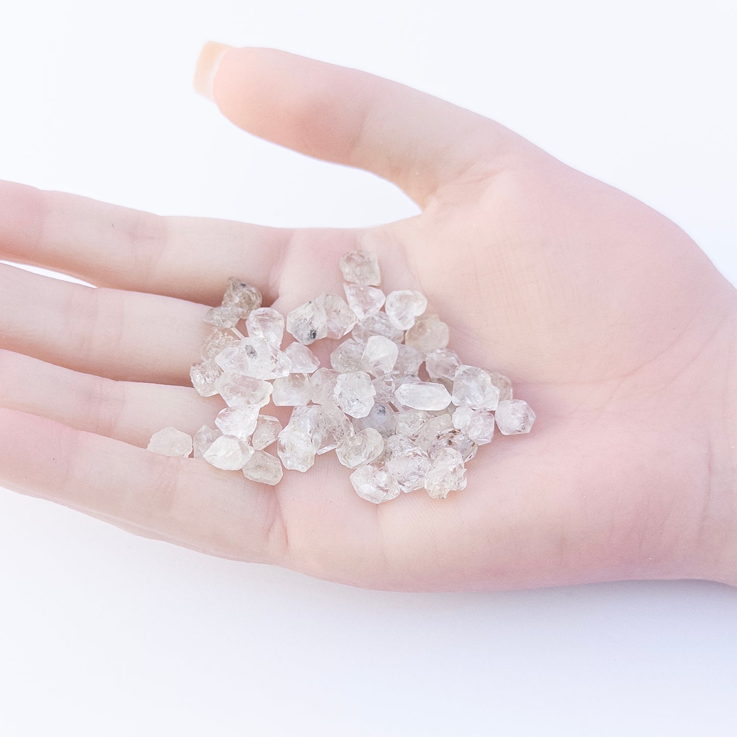 A person holds delicate pieces of Herkimer Diamonds rough, showcasing their raw crystal design.