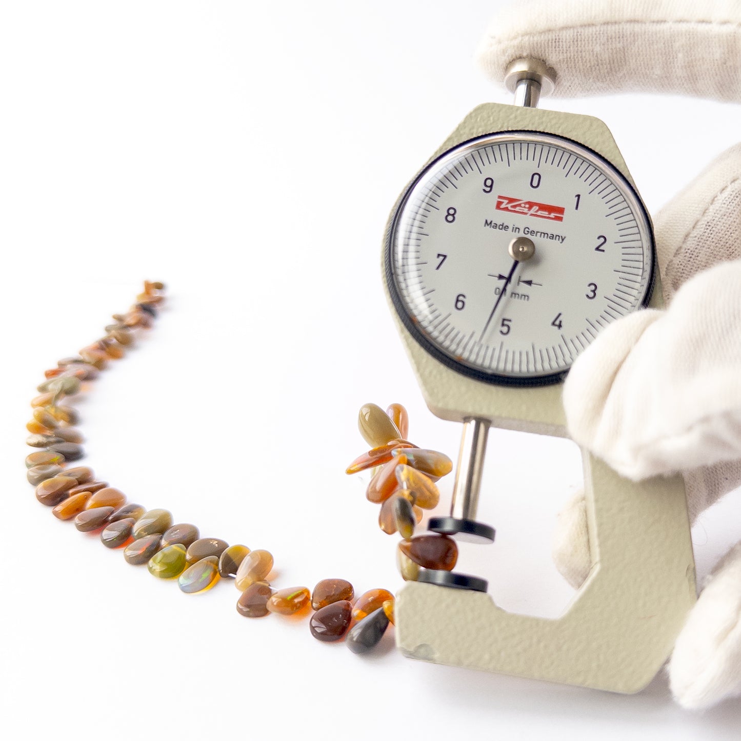 A dial gauge measures the Ethiopian Opal smooth briolette 4–8mm gemstone.  