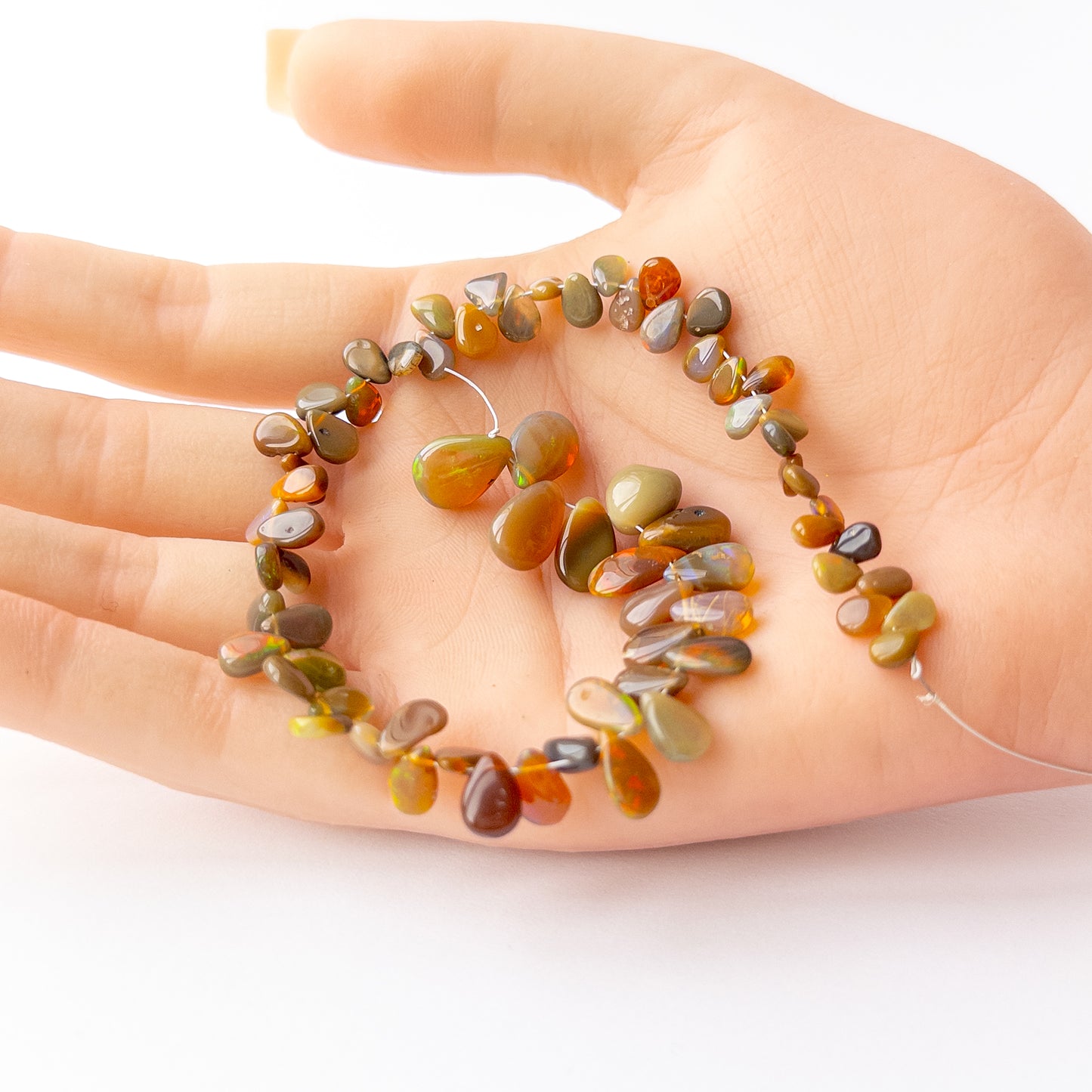 A person holds delicate strands of Ethiopian Opal beads, showcasing their smooth briolette design.  