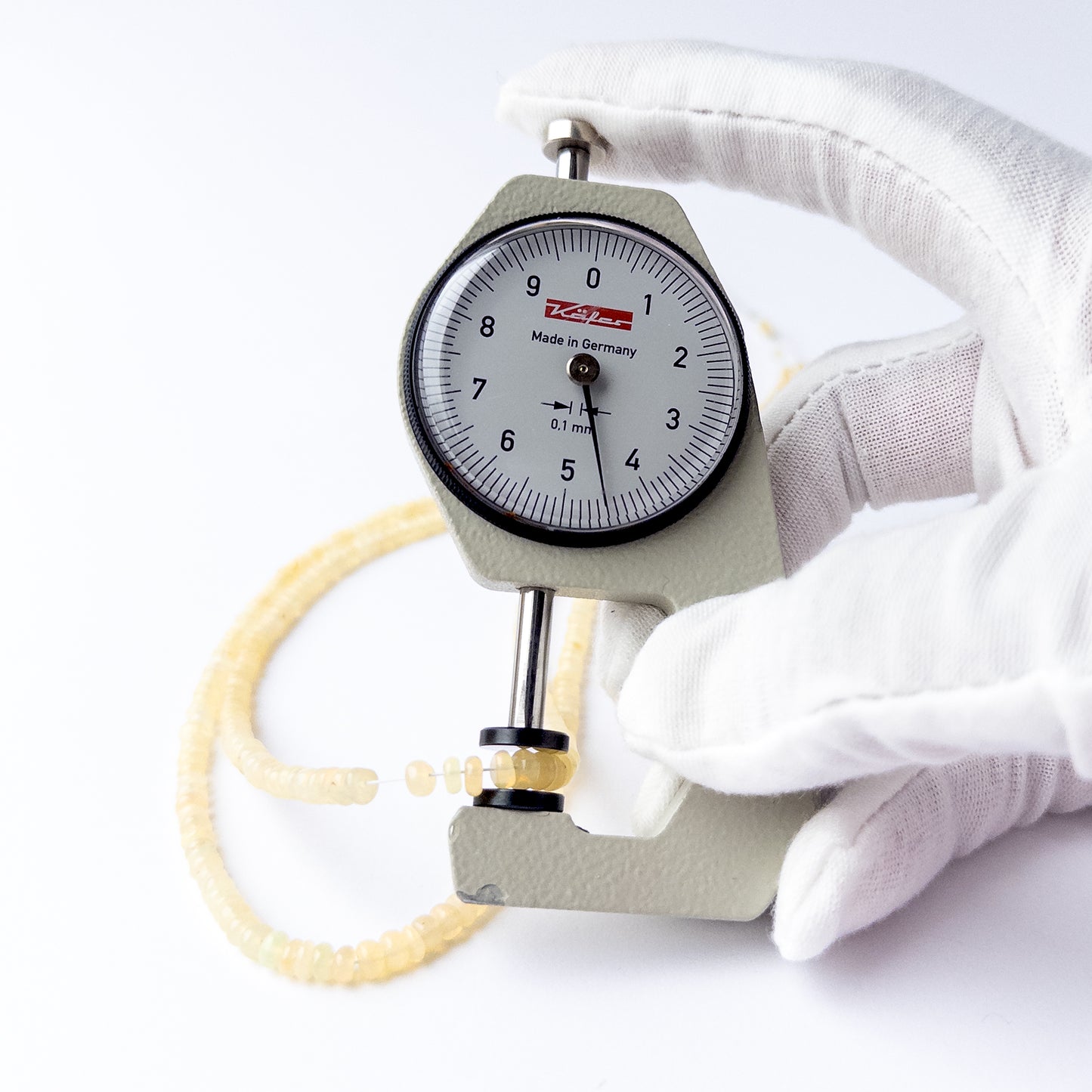 A dial gauge measures the Ethiopian Opal smooth rondelle 3–4mm gemstone.