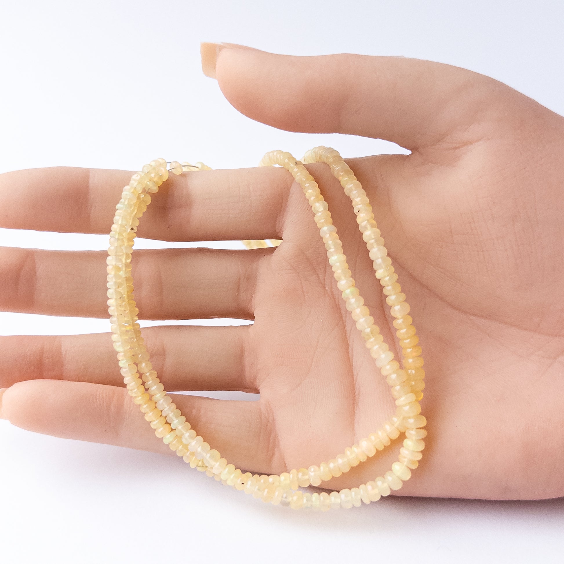 A person holds delicate strands of Ethiopian Opal beads, showcasing their smooth rondelle design.