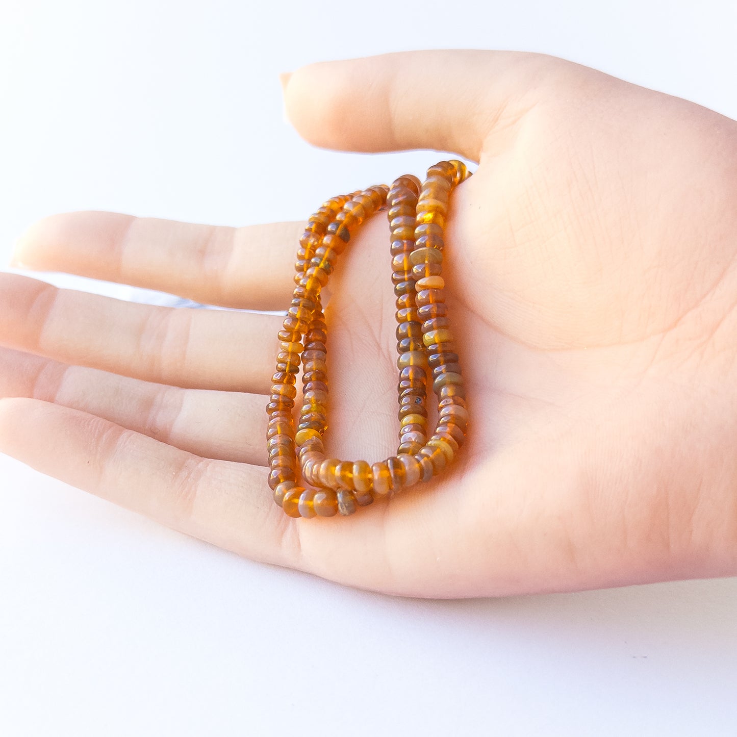 A person holds delicate strands of Ethiopian Opal beads, showcasing their smooth rondelle design.