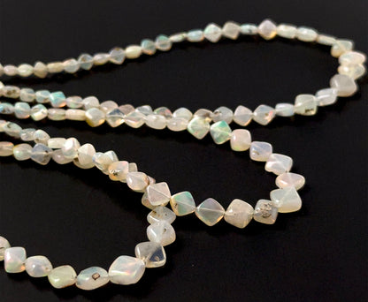 Ethopian Opal smooth rhombus beads sized 3.5–6.5mm arranged in a 44cm strand, showing soft milky tones with flashes of colour and a polished finish.