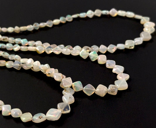 Ethopian Opal smooth rhombus beads sized 3.5–6.5mm arranged in a 44cm strand, showing soft milky tones with flashes of colour and a polished finish.