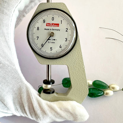 A dial gauge measures the oval pearl gemstone.