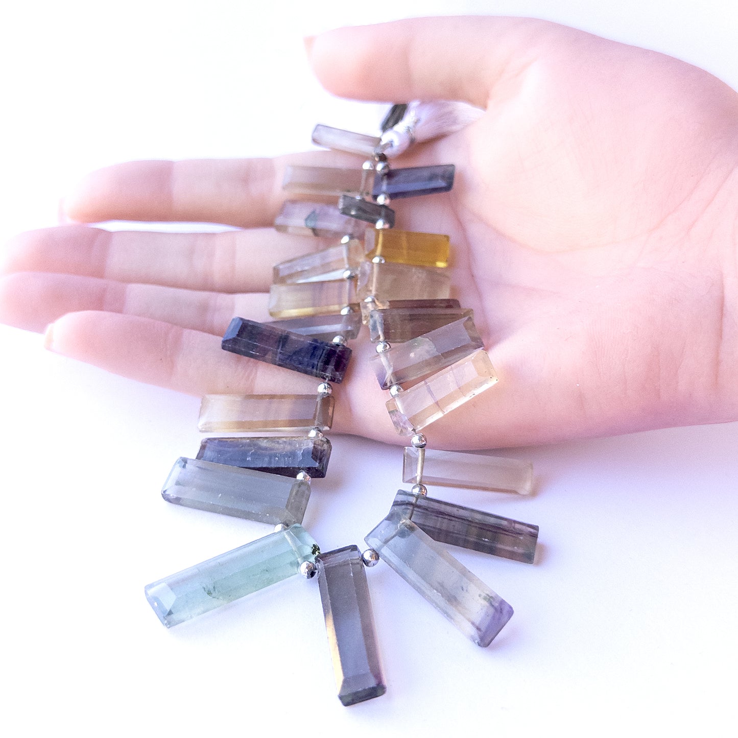 A person holds delicate pieces of Fluorite beads, showcasing their faceted rectangle design.