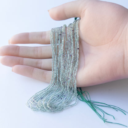 A person holds delicate strands of Fluorite beads, showcasing their Faceted Rondelle design.