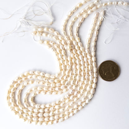 A coin is place near delicate strands of Freshwater Baroque Pearls beads for scale.