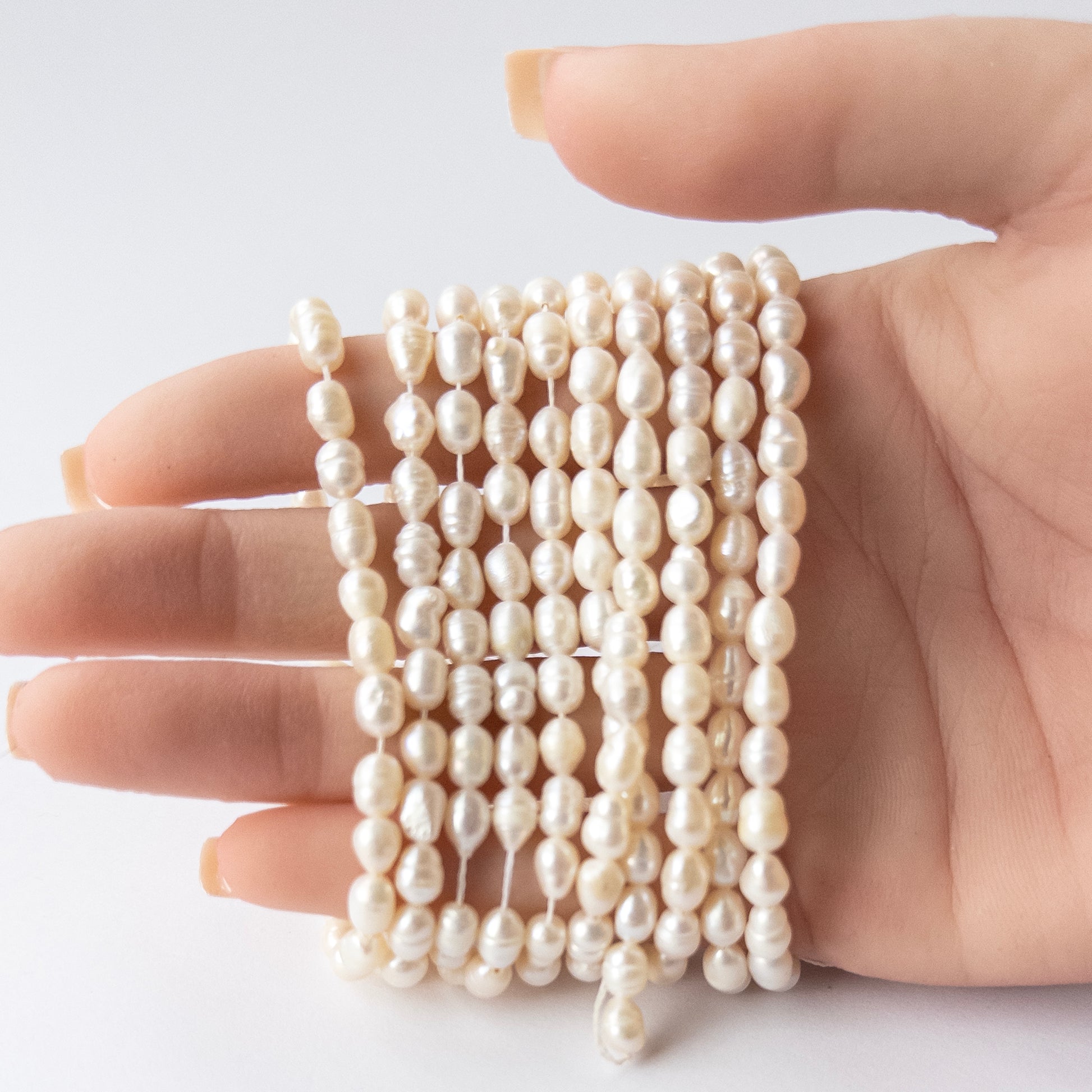 A person holds delicate strands of Freshwater Baroque Pearls beads, showcasing their baroque design.