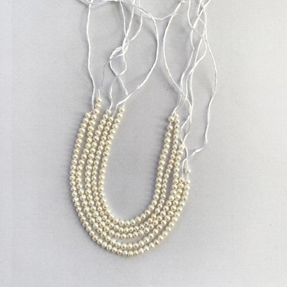 Close-up of smooth round freshwater pearls, 3.0-3.2mm in size, glistening along a 13cm strand.