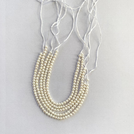 Close-up of smooth round freshwater pearls, 3.0-3.2mm in size, glistening along a 13cm strand.