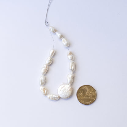 A coin is placed near delicate pieces of freshwater pearls for scale.