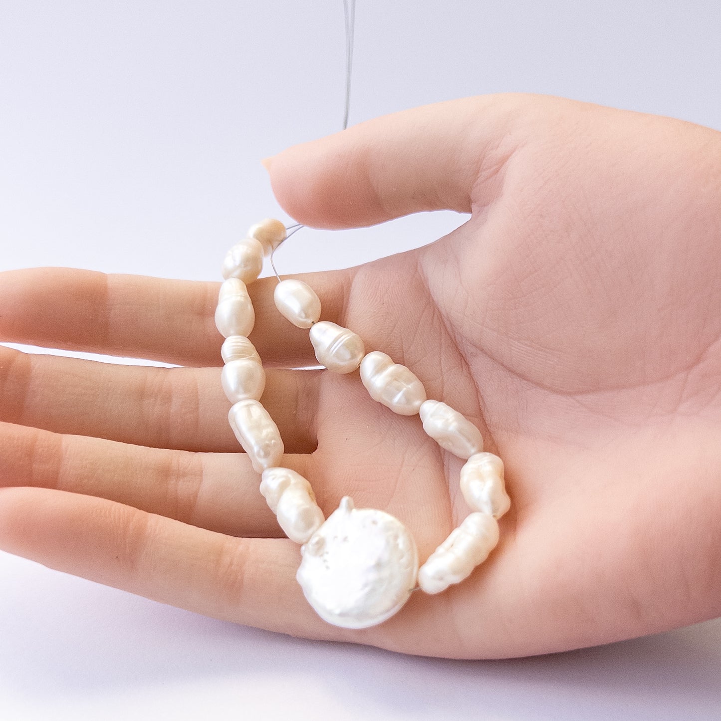 A person holds delicate pieces of freshwater pearls, showcasing their baroque design.