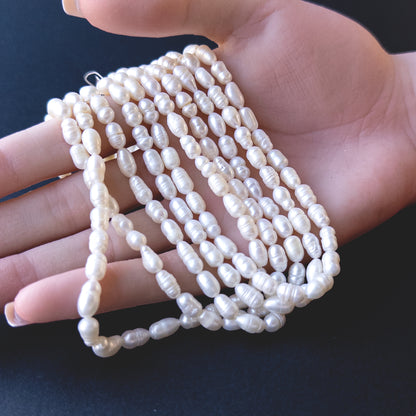 A person holds delicate strands of freshwater baroque pearls, showcasing their rice‑shaped design.
