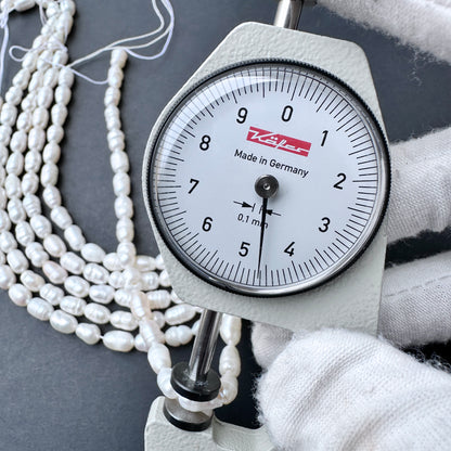 A dial gauge measures breadth of a baroque rice shaped Freshwater Pearl.