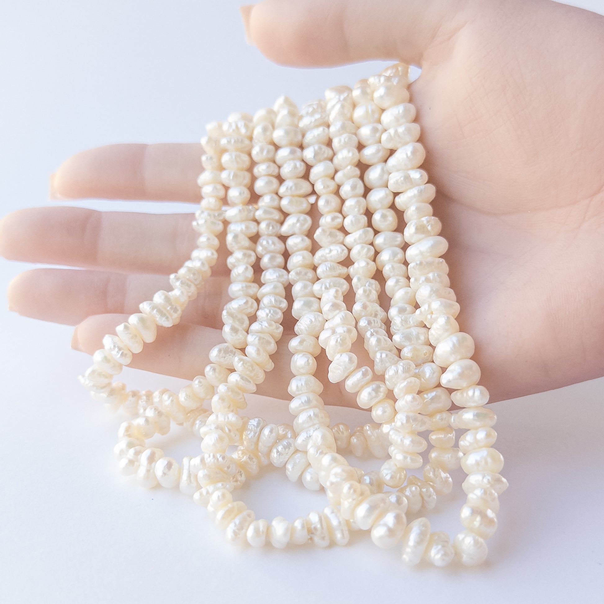 A person holds delicate strands of Freshwater Pearl beads, showcasing their Baroque design.