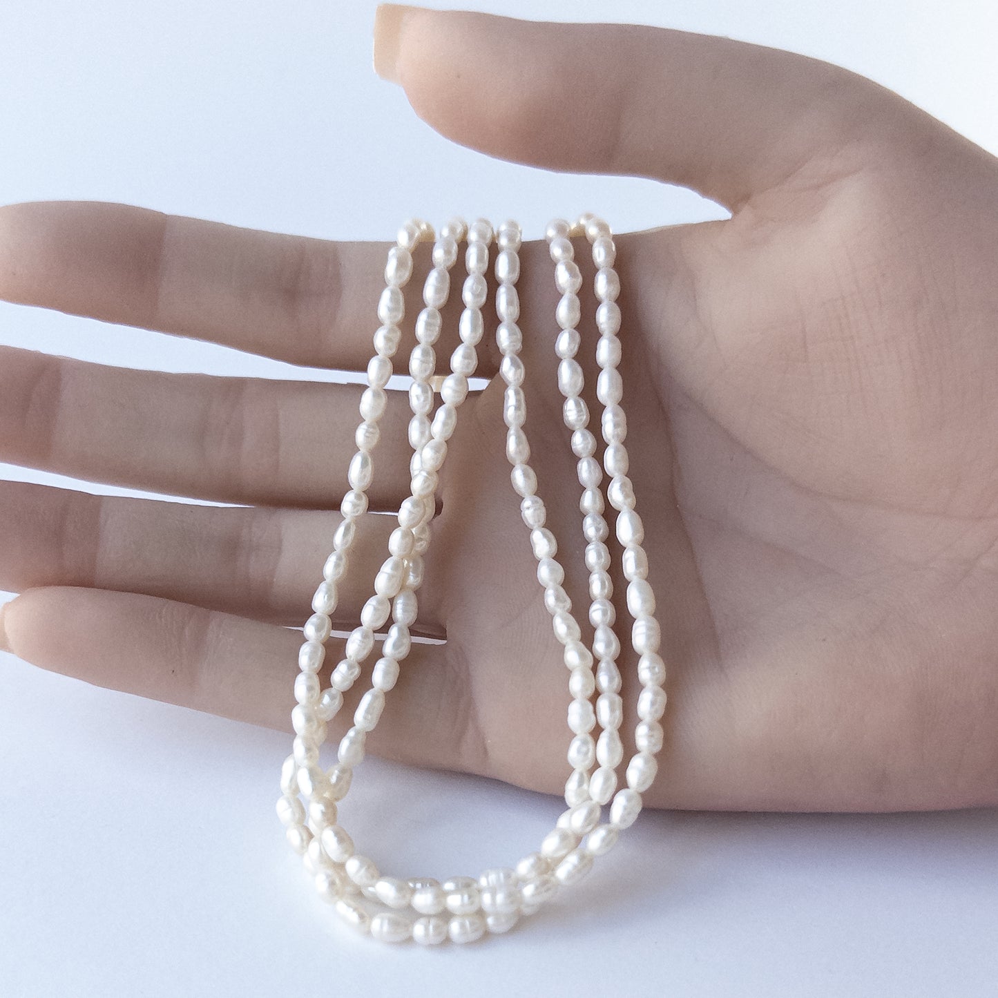 A person holds delicate strands of Freshwater Pearls beads, showcasing their fancy oval design.