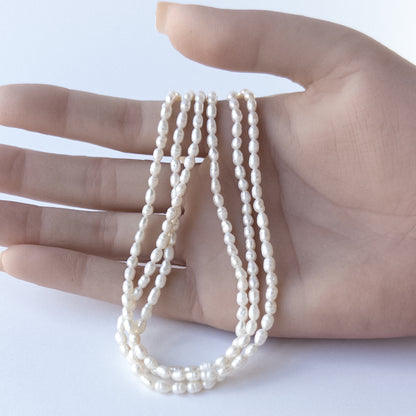 A person holds delicate strands of Freshwater Pearls beads, showcasing their fancy oval design.