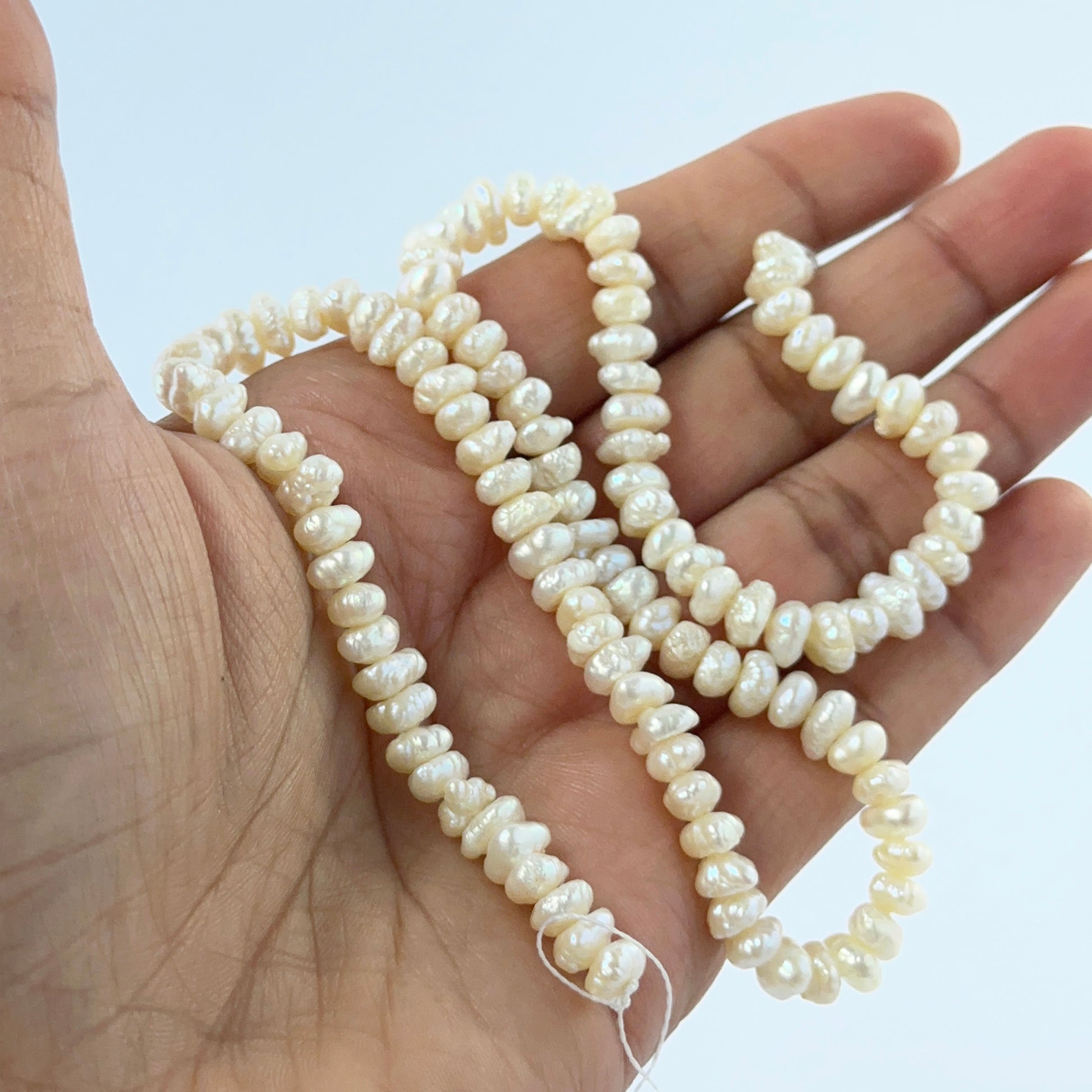 A person holds delicate strands of Freshwater Pearl beads, showcasing their smooth design.
